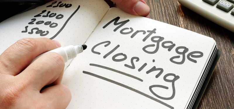 Hands holding a notepad and writing the words Mortgage Closing.