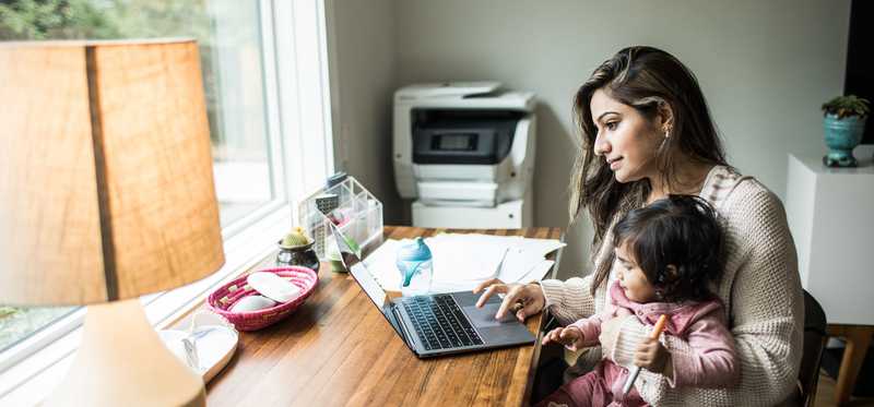 Person with child on lap is working on laptop in home office.