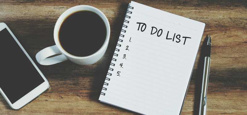 A to-do list, cell phone, cup of coffee, and pen lying on a table.