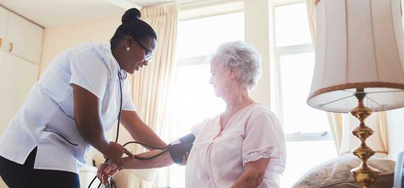 Medical worker checking patient's blood pressure in home setting.