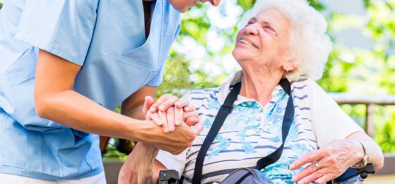Woman in scrubs holding the hand of elderly woman in wheelchair