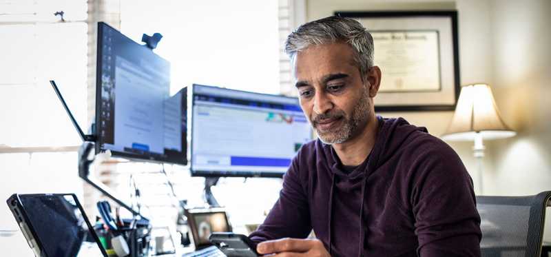 Person using phone at desk with multiple computer monitors.