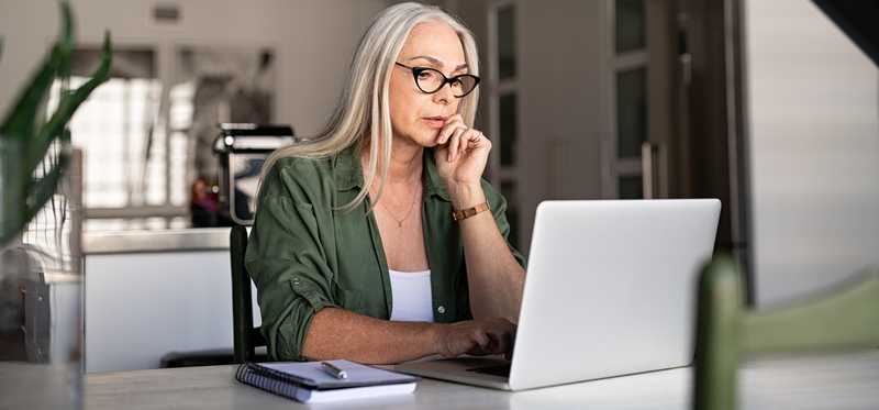 Older woman in glasses is looking at laptop.