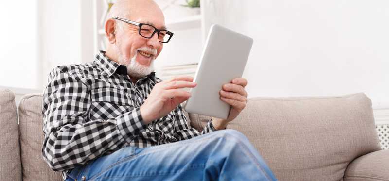 An older man reading tablet on couch.
