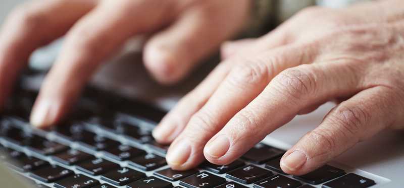 The hands of an older person typing on a keyboard.