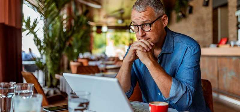 Person sitting in a coffeeshop and looking at laptop.