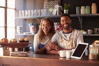 Young smiling couple standing behind coffee shop counter.