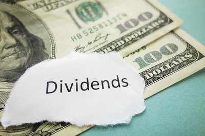 $100 bills with the word "Dividends" on a piece of paper.