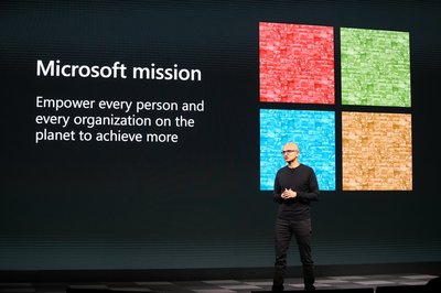 A picture of Microsoft CEO Satya Nadella presenting Microsoft's mission, which is described on a screen behind him alongside the Microsoft logo.