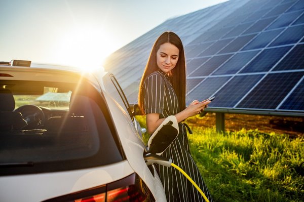 Adult stands outside near solar panels, waiting for her electric car to charge.