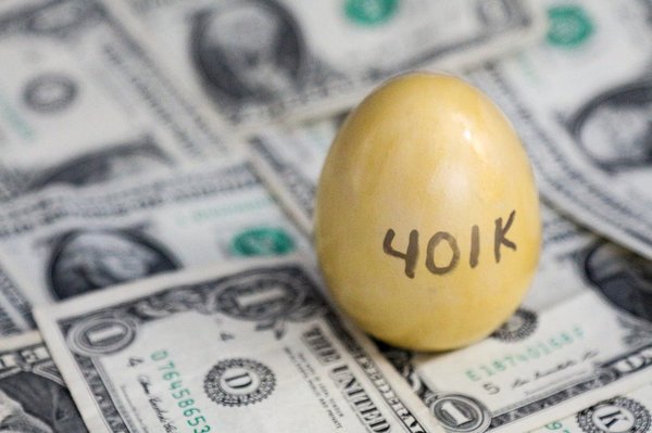 Golden egg with the "401K" written on it stands vertically atop of dollar bills