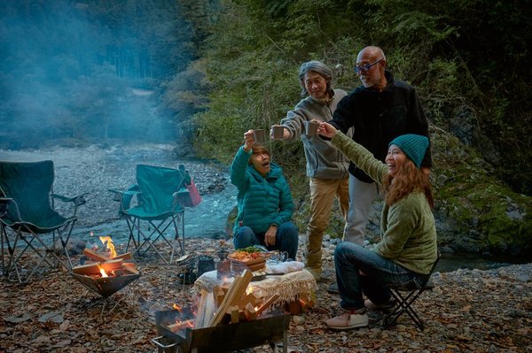 Four people drinking around a campfire in the woods.