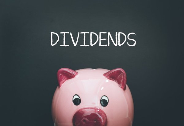 Pink glass piggy bank with "dividends" written above its head on the chalkboard behind it.