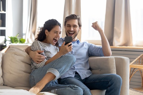 A happy couple looking at a phone and cheering.