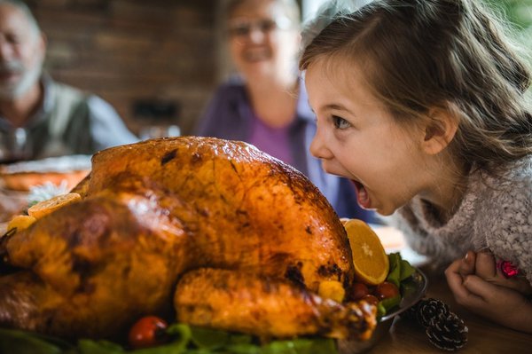 A child playfully pretending to eat a large cooked turkey.