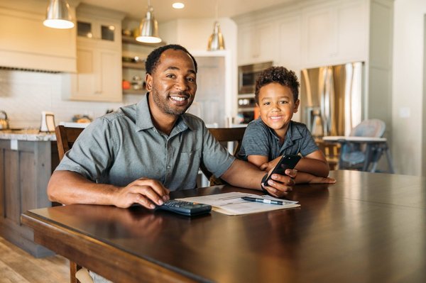 Parent and child at kitchen table using a calculator.