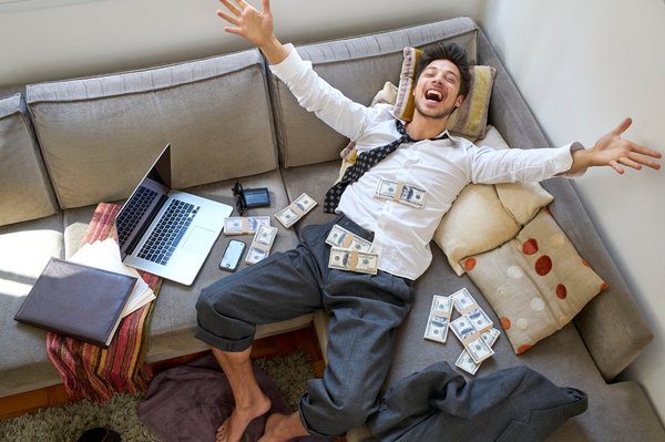 A man lying on a couch covered in cash