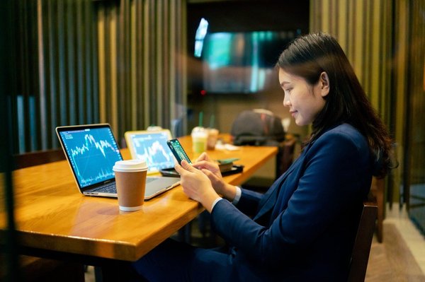A person sits in front of two computers with crypto exchange charts on them.