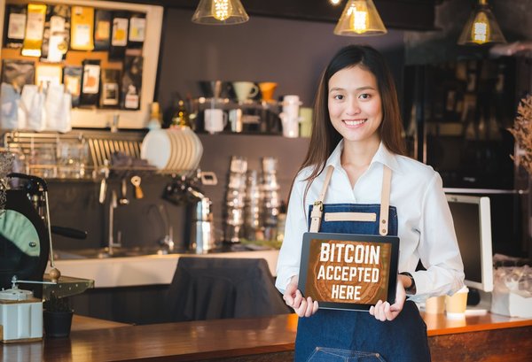 Someone in a cafe holding a sign that reads "Bitcoin accepted here."