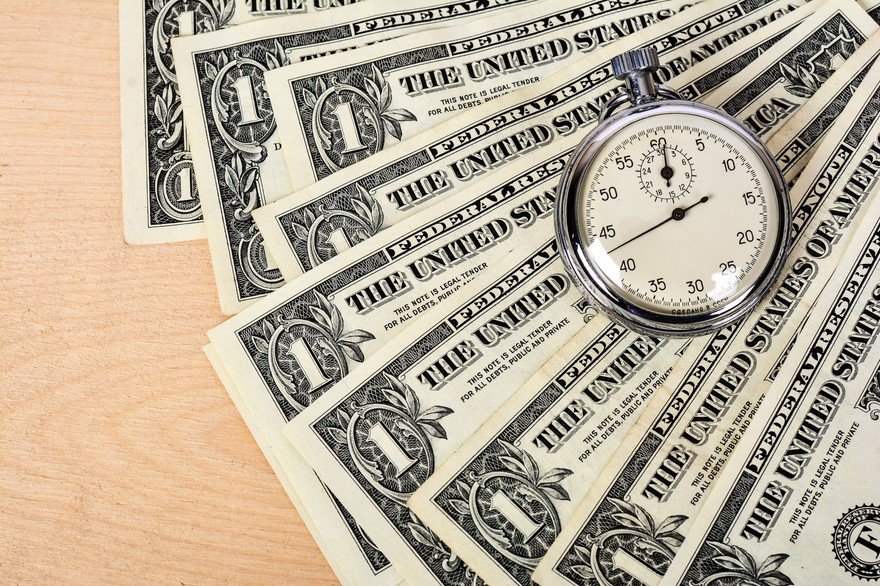 Stopwatch sits on dollar bills on a wooden table.