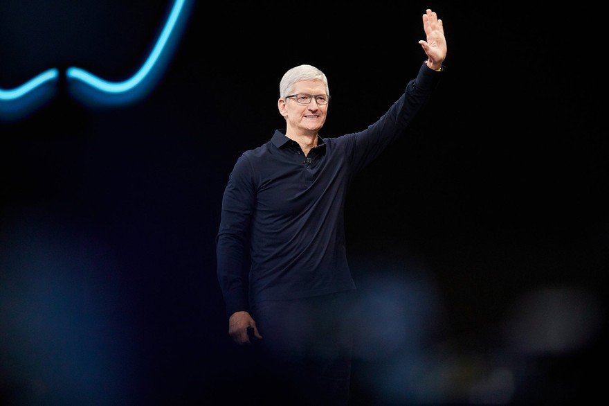 Tim Cook, Apple CEO, waves in front of black background on stage.