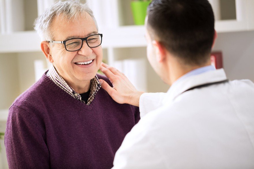 A young doctor touches an older man's shoulder.