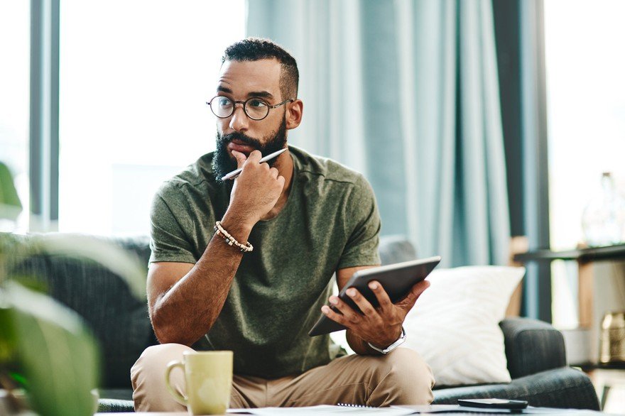 A man holding a tablet and a stylus is thinking.