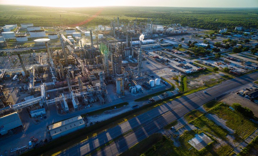 An oil refinery casting shadows as the sun sets in the background.