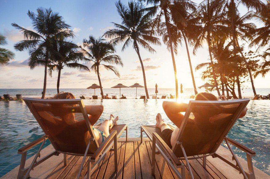 Two people look out over the ocean from a platform at a tropical resort.