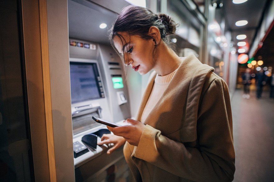 A woman using her phone while scanning fingerprint at ATM.