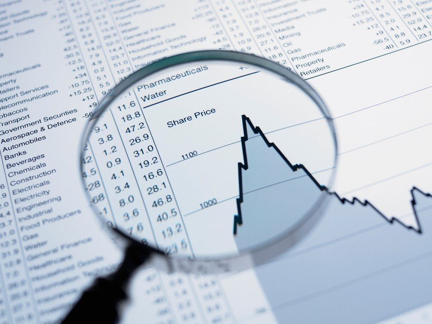 A magnifying glass looking at a stock chart showing an uptrend reversing to a downtrend.