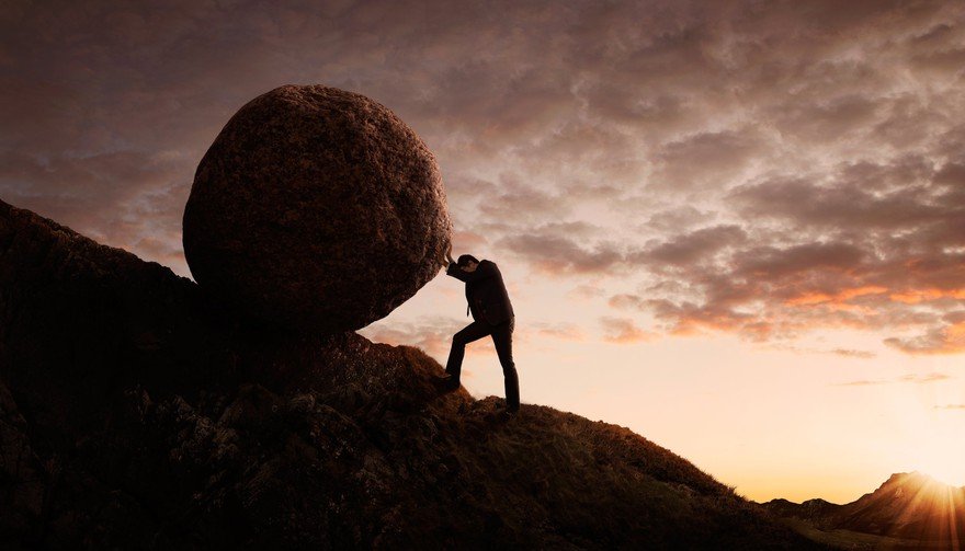 Man pushing a boulder up a hill.