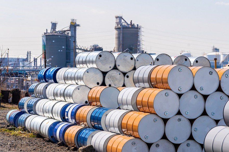Oil barrels stacked high outside a refinery.