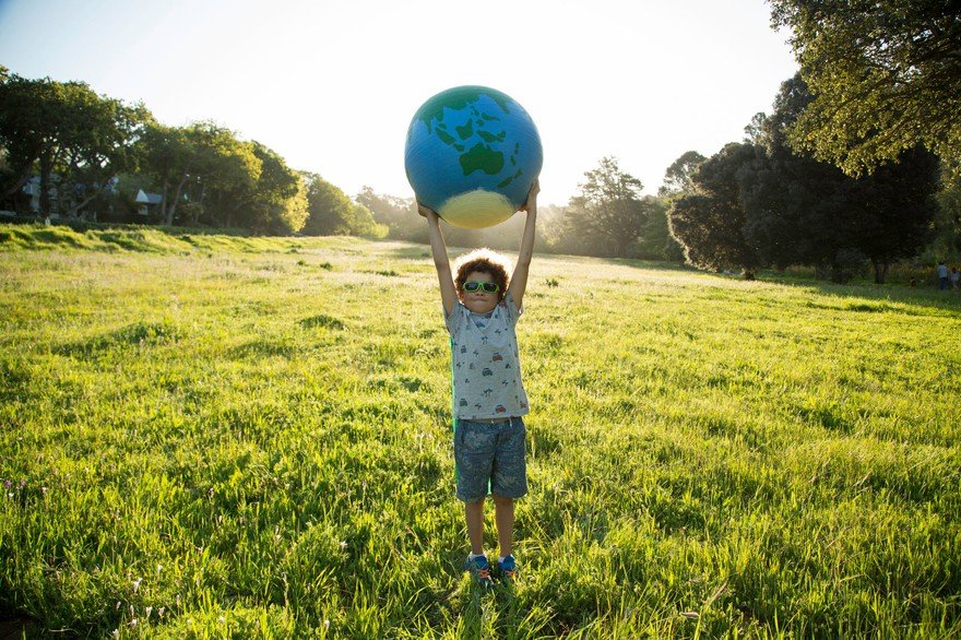 Boy holds up globe in green field.