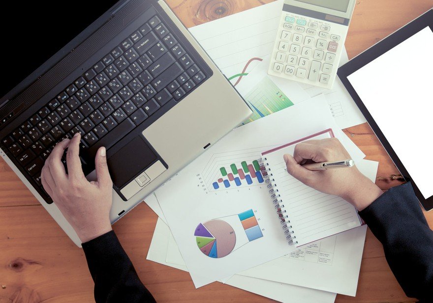 Hands of a person looking at a laptop and financial data.