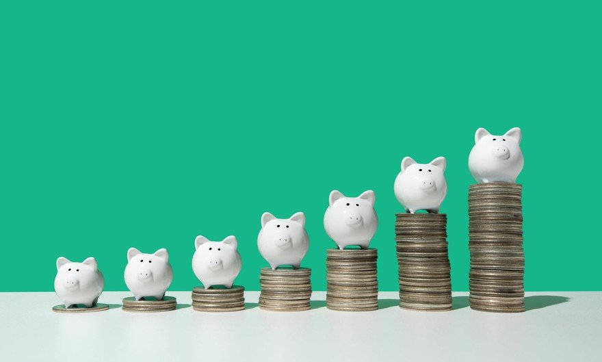 Little white piggy banks standing on top of 7 stacks of coins in ascending order on white surface, green background.