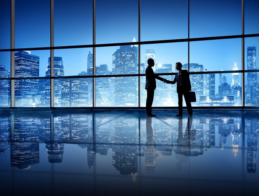 Two people shaking hands with an office skyline in the background.