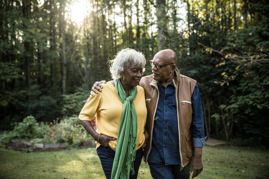 Senior couple walks in woods arm in arm as the sun sets.