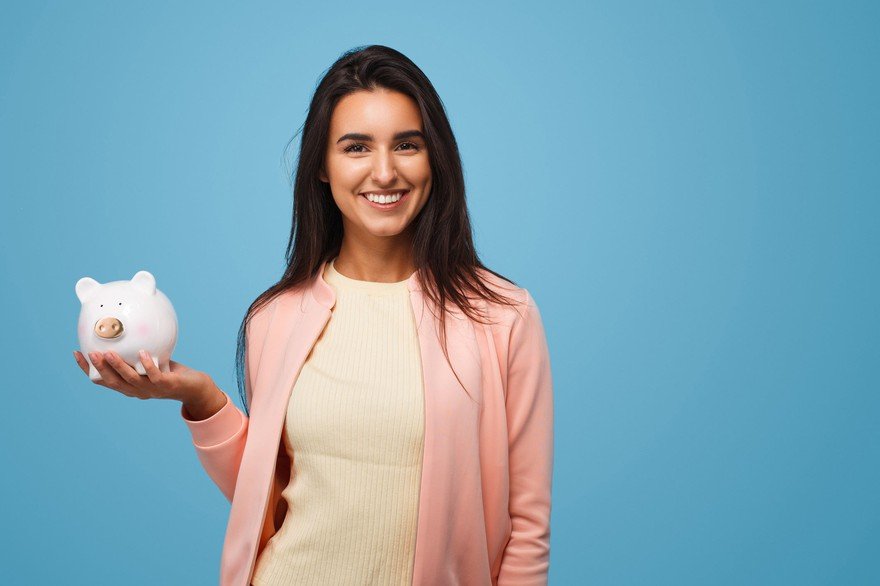 dark haired woman in pink sweater holding a white piggy bank