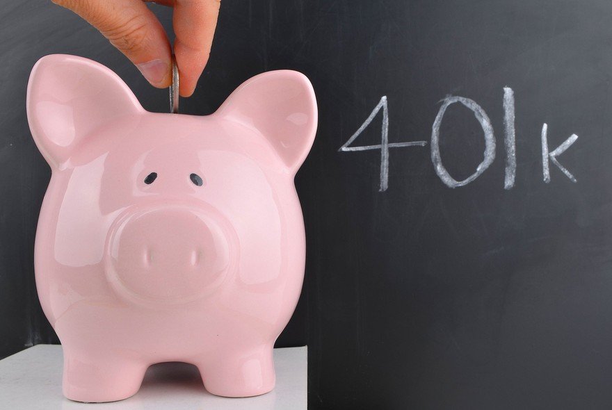 A person putting a coin into a piggy bank. 401k written on a blackboard in the background.