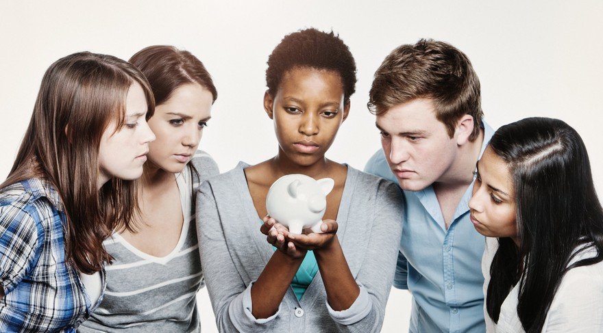 A diverse group of young people gather around a piggy bank.