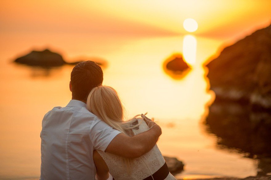 A young couple watching the sunset from a beach.