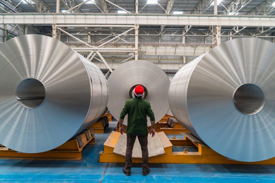 A person looking at giant rolls of aluminum.
