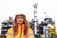 Caucasian woman in white hard hat stands in from of oil equipment