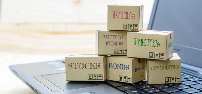 Boxes sitting on laptop keyboard, labeled with types of financial instruments, like REITs, stocks, bonds, and more..