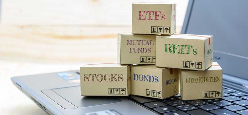 Boxes sitting on laptop keyboard all labeled with types of financial instruments like ETFs, REITs, stocks, etc.