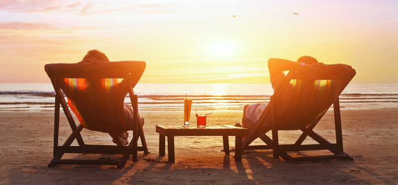 Two people relaxing on beach chairs at sunset.