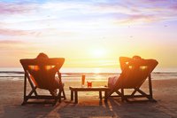 Two people relaxing on beach chairs at sunset.