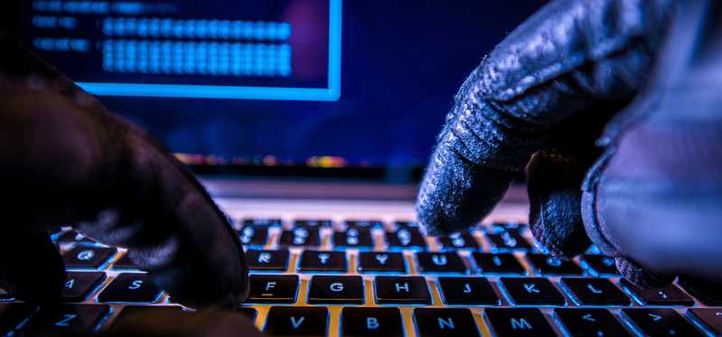 pair of gloved hands typing on laptop keyboard