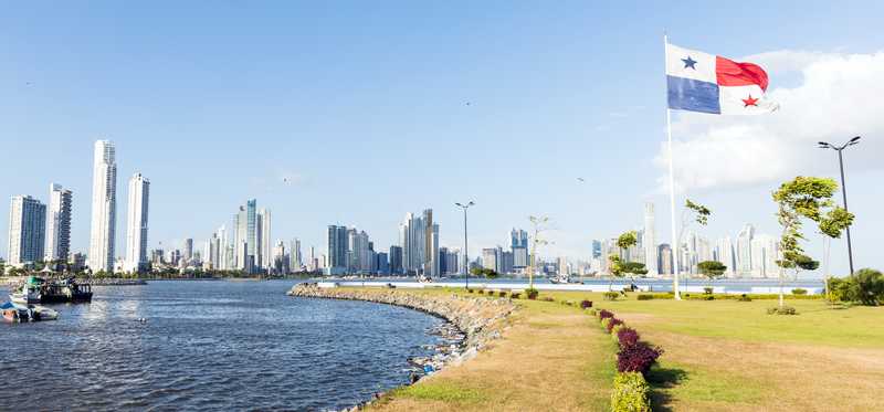 The Panama City skyline with the beach and a Panamanian flag in the foreground.